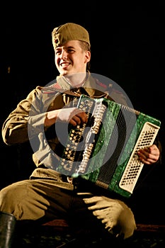 Portra Soviet soldier, hero in uniform of World War II playing the accordion over black background.