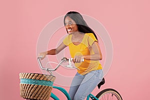 Portraif of pretty black lady riding vintage bicycle on pink studio background