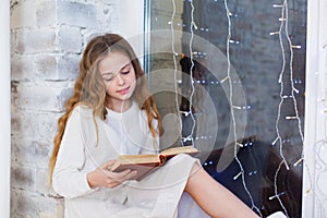 Portrait of 10 years old child reading book on the window on christmas.