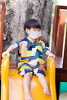 Portrait of A 2-3 years old child wear a white medical face mask. Little boy is playing yellow slides. Son`s leisure activities.