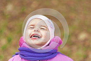 Portrait of 2-3 years old girl in pink warm autumn clothes and violet scarf crying with closed eyes. Expression of fear and pain