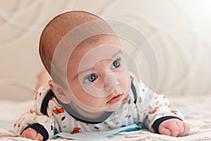 portrait of 2 months old adorable baby boy with big blue eyes and long eyelashes. cute baby lying on his stomach and looks away