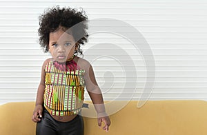 Portrait of a 2-year-old Nigerian girl with beautiful curly hair standing on a sofa.