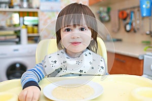 Portrait of 2 years little child eating wheat porridge with pump