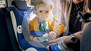Portrait of 2 years old baby boy sitting in car safety seat and holding a toy