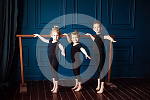 Portrait of 3 little children two girls ballerina and small boy dancer in black leotard practicing at ballet barre at dance studio