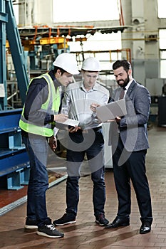 Portrait of a 3 men in a airplane manufactory. Two company managers and one factory worker deciding future plans.