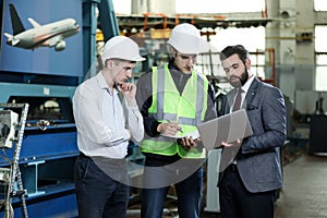 Portrait of a 3 men in a airplane manufactory. Two company managers and one factory worker deciding future plans.