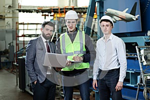 Portrait of a 3 men in a airplane manufactory. Two company managers and one factory worker deciding future plans.