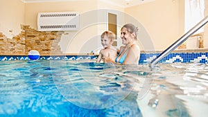 Portrait of 3 years old toddler boy with young mother swimming in the indoors pool. Child learning swimming and doing