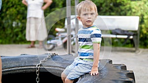 Portrait of 3 yeas old toddler boy witting on the big rubber tire at children playground in park
