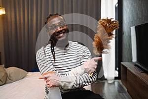 Portrait of 30s African guy holding a feather duster ready for cleaning his apartment