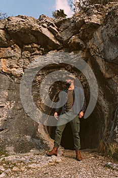 Portrait of a 30s man with a fedora and shirt at the entry of the Homer`s cave