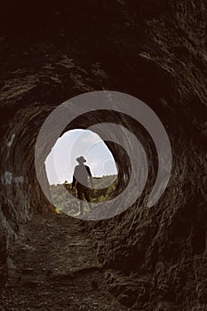 Portrait of a 30s man with a fedora and shirt at the entry of the Homer`s cave