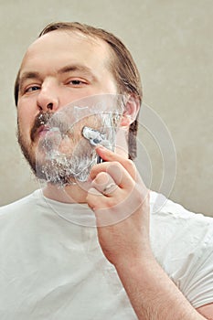 Portrait of a 35-40 year old man shaving his beard with a razor, close-up. Concept of self-cutting and shaving during the flu