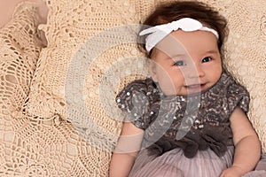 Portrait of a 4 month cute baby girl, wearing white headband and grey dress, lying down on a bed pillows
