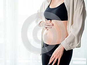 Portrait of 4 months pregnant Asian woman in white bed room, Woman touching her abdomen belly on white background.