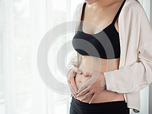 Portrait of 4 months pregnant Asian woman in white bed room, Woman touching her abdomen belly on white background.