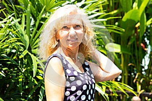 Portrait of a 50-year-old woman in summer against a background of green tropical palm trees.