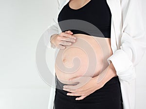 Portrait of 6 months pregnant Asian woman in white bed room, Woman touching her abdomen belly on white background.