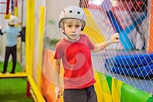 Portrait of 6 years old boy wearing helmet and climbing. Child in abstacle course in adventure playground