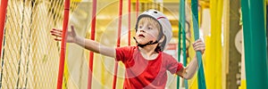 Portrait of 6 years old boy wearing helmet and climbing. Child in abstacle course in adventure playground BANNER, LONG