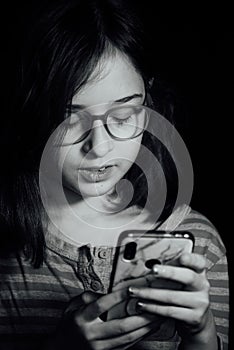 Portrait of a 9 years old female child with black background dark, portrait concept of a child. Girl with a phone