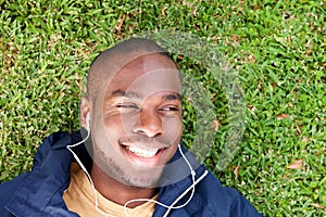 Above of happy young black man lying on grass listening to music with earphones