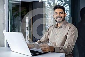 Portrait of accountant financier at workplace, businessman with laptop smiling and looking at camera inside office at