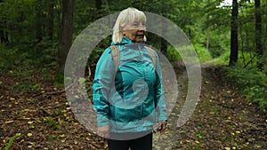 Portrait of active 50s senior woman with backpack on hike through woodland countryside walking into frame breathing in