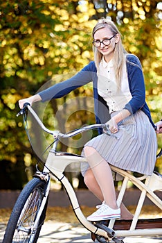 Blond long-haired attractive girl on pink lady bicycle in sunny autumn park on trees background.