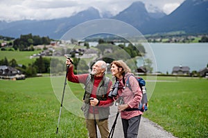 Portrait of active elderly couple hiking together in mountains. Senior tourists walking with trekking poles.