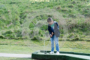 Portrait active kid playing mini golf in the park, Cute young boy doing outdoor activity playing crazy golf in the Spring field,