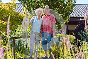 Portrait of an active senior couple holding gardening tools in the garden