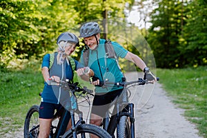 Portrait of active senior couple riding bicycles at summer park, looking at sports smartwatch, checking their