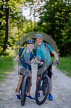 Portrait of active senior couple riding bicycles at summer park, standing on path and looking at camera