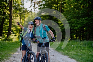 Portrait of active senior couple riding bicycles at summer park, standing on path and looking at camera