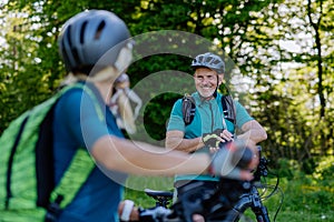 Portrait of active senior couple riding bicycles at summer park, standing on path and looking at camera