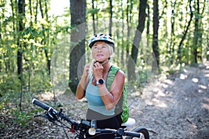 Portrait of active senior woman biker putting on helmet outdoors in forest.
