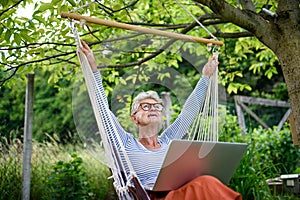 Portrait of active senior woman with laptop working outdoors in garden, home office concept.
