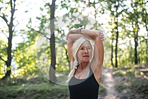 Portrait of active senior woman runner stretching outdoors in forest.