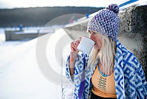 Portrait of active senior woman sports clothes drinking tea outdoors in winter, cold therapy concept. Copy space.