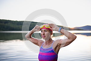 Portrait of active senior woman swimmer outdoors by lake.