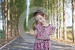 Portrait of adorable 5 years old asian posting for her cute face in beautiful park with perspective view of concrete road as