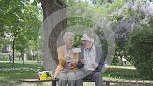 Portrait adorable adult couple looking old photos remembering happy moments sitting on a bench in the park. Mature