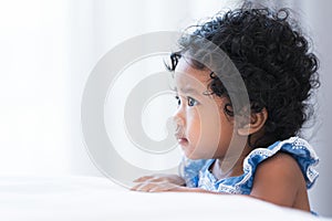 Portrait of adorable African 7 months old newborn baby girl with black curly hair standing near bed at home, looking forward