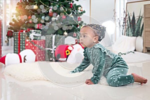 Portrait of adorable African American little girl child climbing on white carpet at living room floor with many gift boxes
