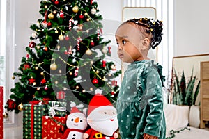 Portrait of adorable African American little girl child standing in living room with many gift boxes presents under Christmas tree