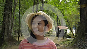 Portrait of adorable asian girl wearing straw hat smiling and walking leisurely in the forest park.