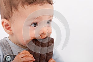 Portrait of an adorable baby boy eating a plate of chocolate.